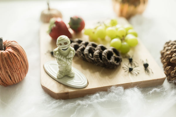 mummy mini on small wood board with chocolate covered pretzels, grapes and strawberries