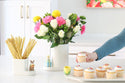 tulip mini on a octagonal platter with cupcakes, stack of presents on the utensil crock filled with flowers and bunny on a cutie container filled with straws