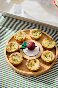 radish mini on top of a round wood board that is filled with quiche and laying on top of a striped tablecloth background.