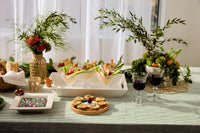 spring table setting with a foxy lady mini, napkin holder, rectangle white tray, digging it terracotta pot mini, round wooden board with a radish mini and two glasses of red wine.