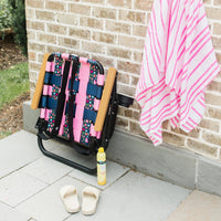 ParkIt Chair with the signature Nora fleming pattern with a cooler and drink holder next to sunscreen, a towel, slides