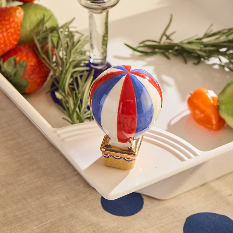 Decorative hot air balloon on a white surface with strawberries and rosemary in the background.