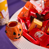 Halloween-themed candy and a small pumpkin-shaped mini on a white plate with a colorful background.