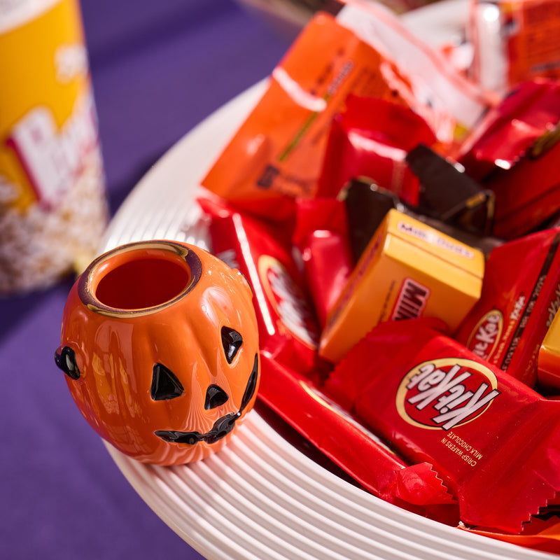 Halloween-themed candy and a small pumpkin-shaped mini on a white plate with a colorful background.