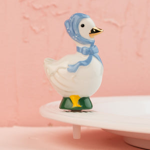 Decorative duck figurine with a blue bow on a pink background