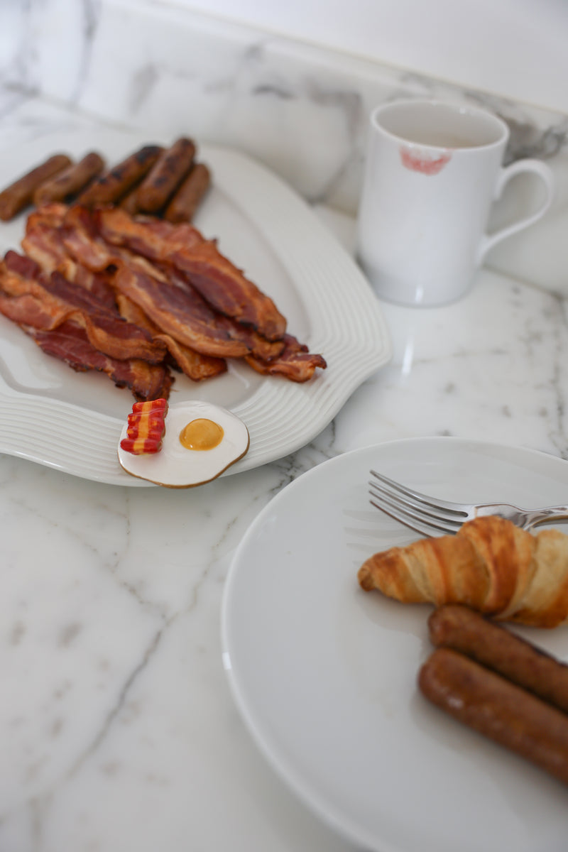 Breakfast setting with bacon, croissant, and sausages on a marble surface.