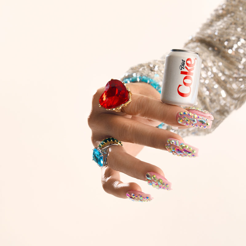 Hand with colorful nails holding a Diet Coke can mini against a light background