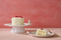 White cake with strawberries on a platter with nora fleming minis, on a pink background