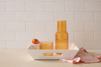 Orange glassware on a white tray with a white tiled wall background