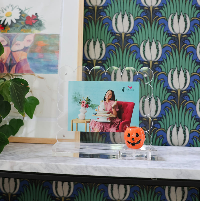 Decorative shelf with framed pictures against a patterned wallpaper.