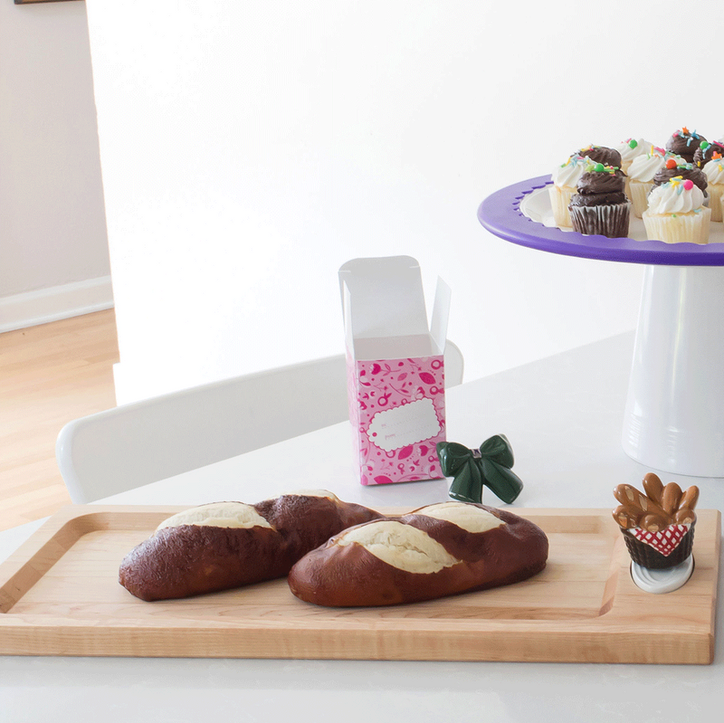 This image features a handcrafted maple bread board designed by J.K. Adams with a bread basket mini, a round platter with black cat mini, gumball mini on a round platter sitting on a high riser.