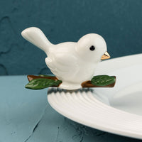 White ceramic bird mini on a branch with a blue background