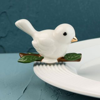 White ceramic bird mini on a branch with a blue background