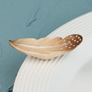 creative quill mini is a brown feather mini with white dots on a round white platter and a blue background.