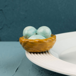 Three turquoise ceramic eggs in a brown basket on a textured surface mini with a blue background