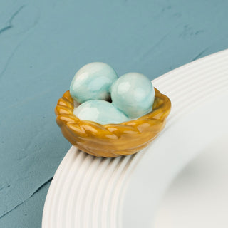 Three turquoise ceramic eggs in a brown basket on a textured surface mini with a blue background