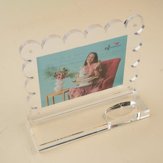 Decorative photo frame with a woman in a pink dress sitting on a red chair, holding nora fleming products.