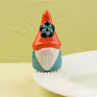 Small gnome mini with an orange hat and blue body on a white plate against a light green background