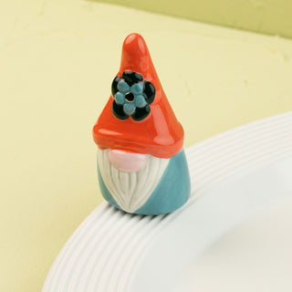 Small gnome mini with an orange hat and blue body on a white plate against a light green background
