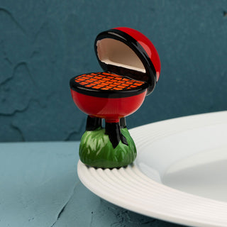 red barbecue grill mini on a green base with a white plate against a blue wall.