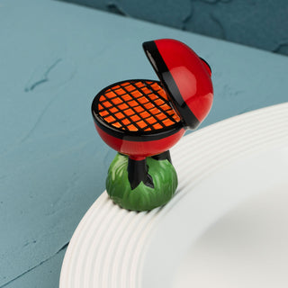 red barbecue grill mini on a green base with a white plate against a blue wall.