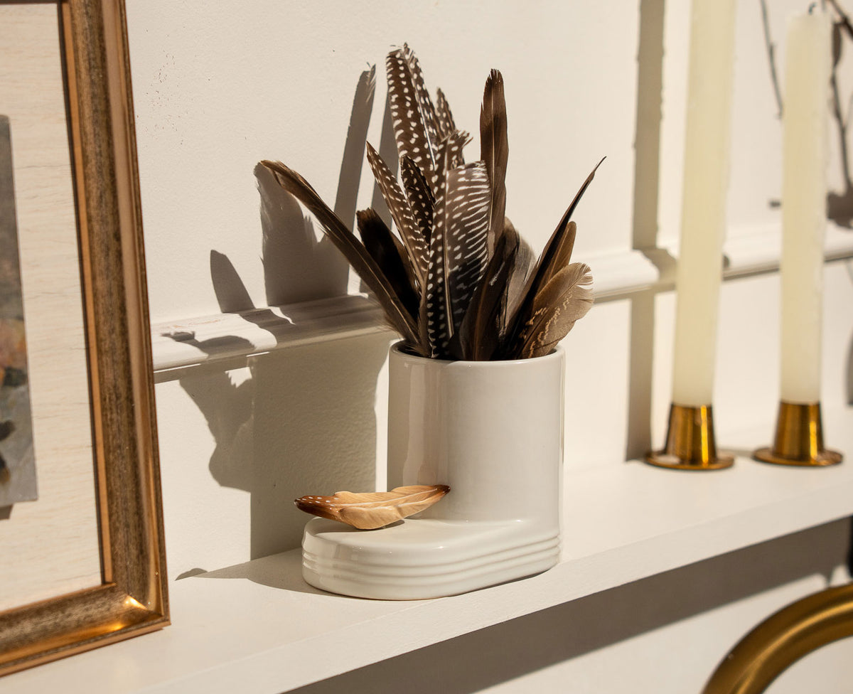 cutie container filled with feathers on a shelf with candles and a mirror in the background