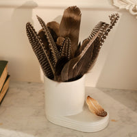 White utensil holder with feathers on a marble surface. The feather "creative quill" mini is in a white utensil holder.