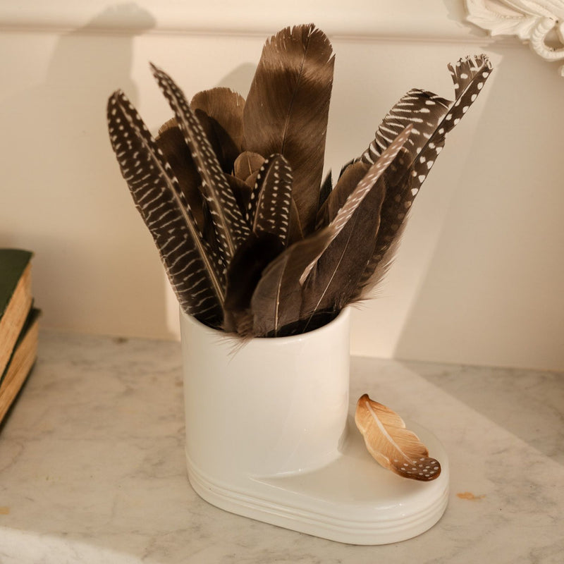 White utensil holder with feathers on a marble surface. The feather "creative quill" mini is in a white utensil holder.