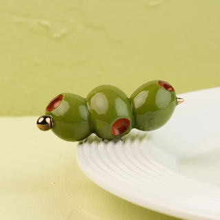 Three green olive-shaped mini with red spots and gold accents on a white surface.