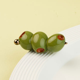 Three green olive-shaped mini with red spots and gold accents on a white surface.