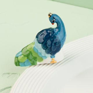 Decorative peacock figurine on a white surface with a light green background