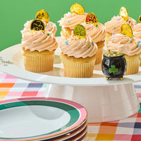 Black pot with a green clover mini on a white surface with cupcakes against a  green background and plaid tablecloth