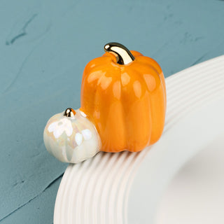 Two ceramic pumpkins, one orange and one white mini, on a white plate against a teal background.