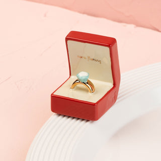 Gold ring with a blue gemstone in a red box mini on a pink background