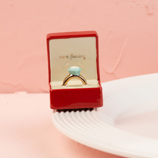 Gold ring with a blue gemstone in a red box mini on a pink background