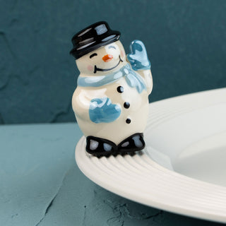 snowman mini with a black top hat, blue scarf, and gloves on a white plate against a teal background.