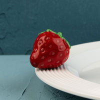 Red strawberry-shaped mini on a white plate against a blue background