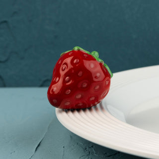 Red strawberry-shaped mini on a white plate against a blue background