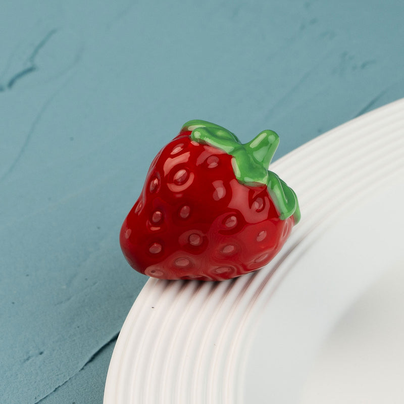 Red strawberry-shaped mini on a white plate against a blue background