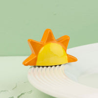 Sun-shaped mini with orange and yellow gradient on a white surface with a light green background