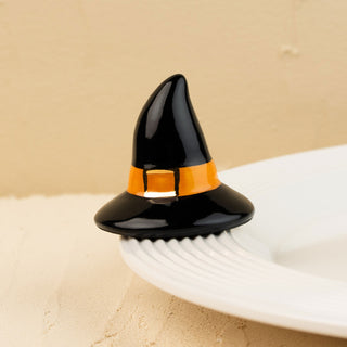 Black witch hat with orange band on a white plate against a beige background